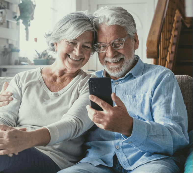 Casal de idosos olhando para o celular e sorrindo.